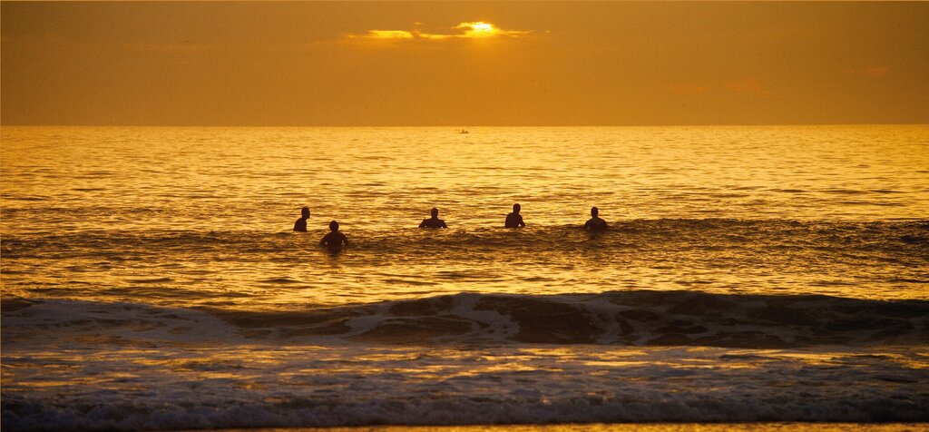 Surfistas no mar apreciando o p&ocirc;r do sol